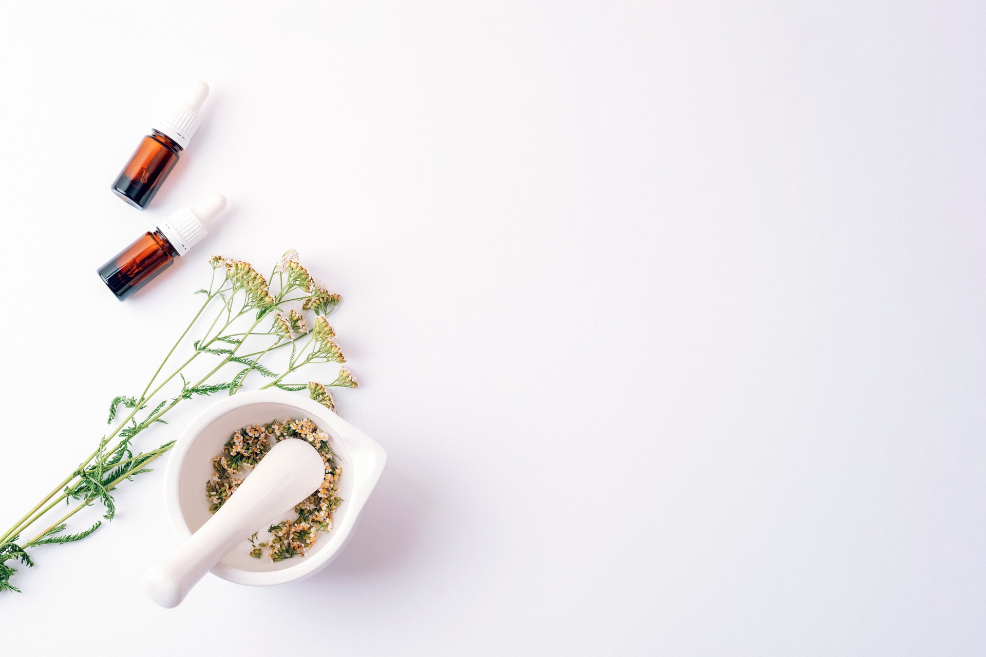 Herbal cosmetic set with essential oil bottles, dried yarrow flowers and mortar on white background. Top view, flat lay, copy space Herbal cosmetic set with essential oil bottles, dried yarrow flowers and mortar on white background. Top view, flat lay, copy space